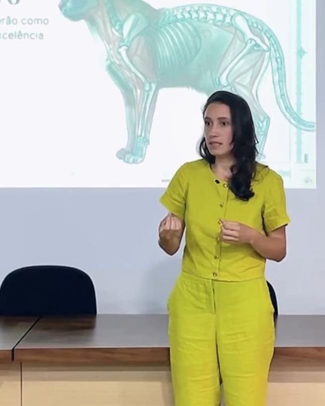 Dra. Alana Castro de pé, falando, diante de uma projeção com o esqueleto de um gato.