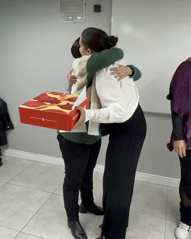 Abraço entre duas pessoas; uma delas sustenta uma caixa.